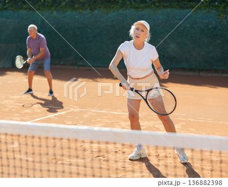 Elderly couple playing tennis together in court Elderly couple playing tennis together in court 136882398