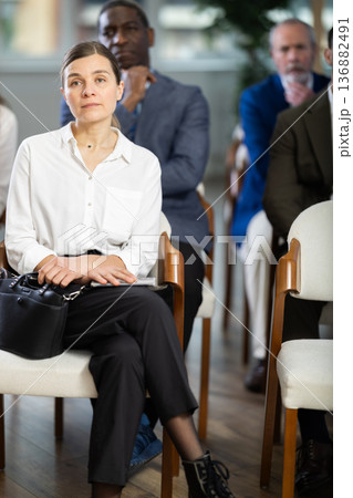 Adult woman listens to presentation in conference room Adult woman listens to presentation in conference room 136882491