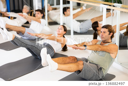 Middle-aged man practicing pilates on gray mat in gym room 136882497