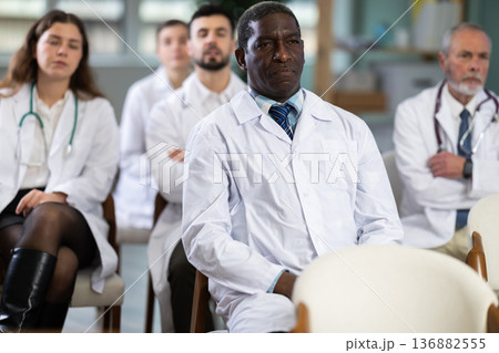 Male doctor listens to lecture with colleagues in auditorium Male doctor listens to lecture with colleagues in auditorium 136882555