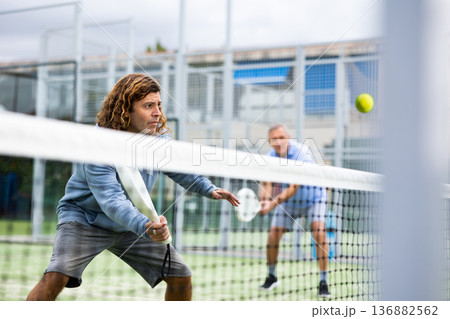 Focused man playing paddleball match on outdoor court 136882562