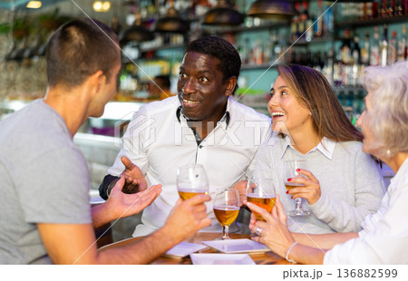 Group of male and female friends chatting and drinking beer. Main focus right in center 136882599
