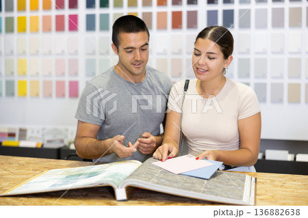 In store, couple buyer look at product catalog and choose color of paint, wall covering in apartment In store, couple buyer look at product catalog and choose color of paint, wall covering in apartment 136882638
