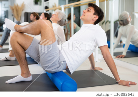 Active vigorous man performs exercises with a pilates roller while on a mat in the hall of a modern fitness studio. 136882643