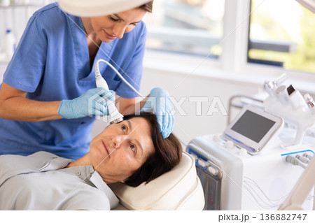 Aged woman receiving facial procedure with high frequency ultrasonic attachment Aged woman receiving facial procedure with high frequency ultrasonic attachment 136882747