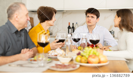 Smiling young man talking with family at festive table with wine and snacks at home Smiling young man talking with family at festive table with wine and snacks at home 136882789