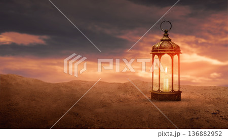 A traditional ornate Arabic fanous lantern with a lit candle glowing on desert sand under a dramatic sunset sky. Ideal for Ramadan, Eid, and spiritual Middle Eastern themes A traditional ornate Arabic fanous lantern with a lit candle glowing on desert sand under a dramatic sunset sky. Ideal for Ramadan, Eid, and spiritual Middle Eastern themes 136882952