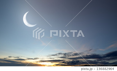 A stunning view of a large, bright crescent moon hanging in the twilight sky over a colorful sunset horizon with soft clouds. Ideal for background or nature-themed projects A stunning view of a large, bright crescent moon hanging in the twilight sky over a colorful sunset horizon with soft clouds. Ideal for background or nature-themed projects 136882964