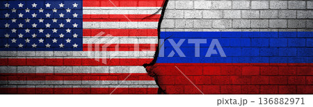 Conceptual image showing American and Russian flags on a cracked brick wall, symbolizing geopolitical tension, conflict, and strained international relations between the two superpowers 136882971