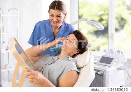 Woman beautician examining face skin of female patient before cosmetology procedure in clinic 136883036