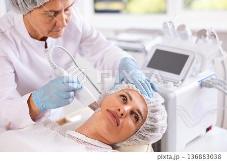 Professional female cosmetologist doing deep cleansing of facial skin of woman in beauty salon 136883038