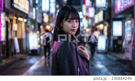 煌びやかな夜の繁華街でレザージャケットを着て振り返る女性 136884249