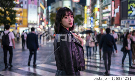 煌びやかな夜の繁華街でレザージャケットを着て振り返る女性 136884251