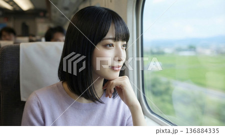 走行中の列車の窓から広がる緑の風景を眺める若い日本人女性の横顔 136884335
