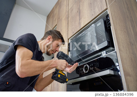 Technician installing built-in microwave oven in modern kitchen cabinet Technician installing built-in microwave oven in modern kitchen cabinet 136884396