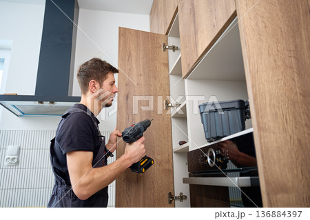 Technician adjusting kitchen cabinet door with cordless drill 136884397