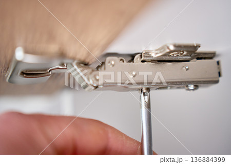 Screwdriver tightening cabinet door hinge, close up Screwdriver tightening cabinet door hinge, close up 136884399