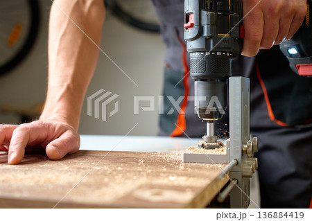 Carpenter drilling wooden board with cordless drill and drilling jig Carpenter drilling wooden board with cordless drill and drilling jig 136884419