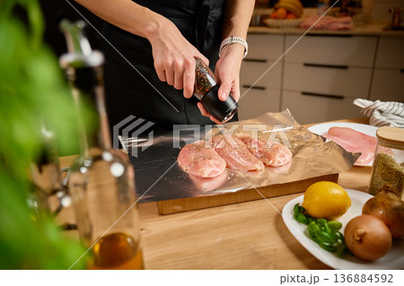Woman seasoning raw chicken fillets on foil at kitchen table Woman seasoning raw chicken fillets on foil at kitchen table 136884592