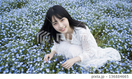ネモフィラの花畑の中でしゃがみ花を優しく触る白いワンピースの女性 136884665