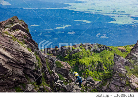 鳥海山・新山山頂を行く登山者と外輪山稜線・庄内平野の眺め 136886162