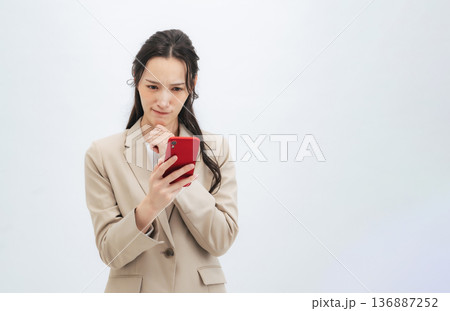 スマホを見ながら悩む女性ビジネスパーソン 136887252