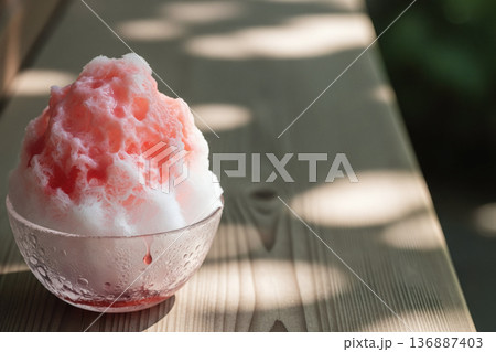 木目調のテーブルに置かれたイチゴシロップのかき氷と木漏れ日 136887403