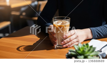 カフェの窓際でアイスカフェラテを持つ女性の手元 136888689