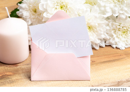 Pink envelope with blank card and white flowers on wooden table 136888785