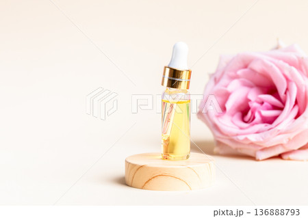 Rose essential oil dropper bottle beside pink rose on wooden base Copy space 136888793