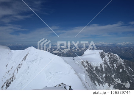 A stunning rock formation covered in snow, set against a clear blue sky with fluffy clouds in the background, creating a peaceful and breathtaking mountain landscape. A stunning rock formation covered in snow, set against a clear blue sky with fluffy clouds in the background, creating a peaceful and breathtaking mountain landscape. 136889744