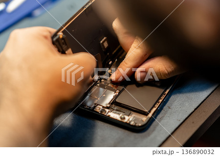Expert Phone Technician Repairs Smartphone Hardware While Focusing on Intricate Components in a Bustling Repair Shop 136890032