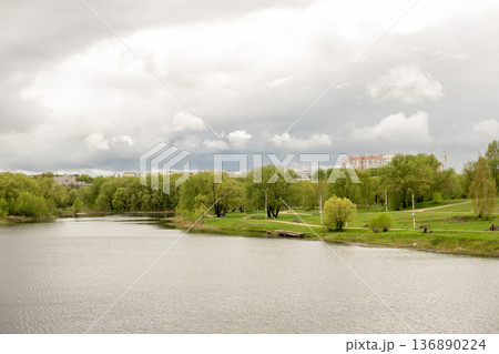 Lush Green Landscape Along a Calm River Under Cloudy Skies During Springtime in a Tranquil Park Setting 136890224