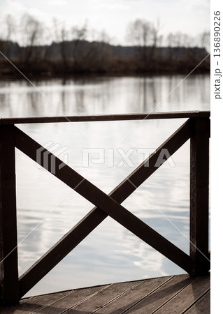 Wooden Railing Overlooking Calm Water Under Soft Cloudy Sky at Dawn 136890226
