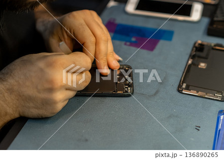 Expert Technician Repairs Smartphone Screen With Precision in a Busy Repair Shop During the Afternoon Hours Expert Technician Repairs Smartphone Screen With Precision in a Busy Repair Shop During the Afternoon Hours 136890265