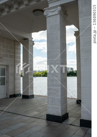 Elegant Architectural Structure Near Water Featuring Tall Columns and Scenic Views Under a Bright Blue Sky With Clouds and Greenery in the Background Elegant Architectural Structure Near Water Featuring Tall Columns and Scenic Views Under a Bright Blue Sky With Clouds and Greenery in the Background 136890315