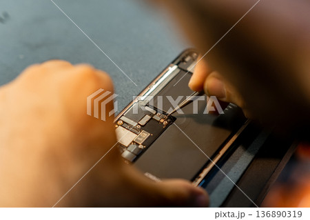 Skilled Technician Performs Phone Repair With Precision Tools During the Day in a Modern Workshop Environment 136890319