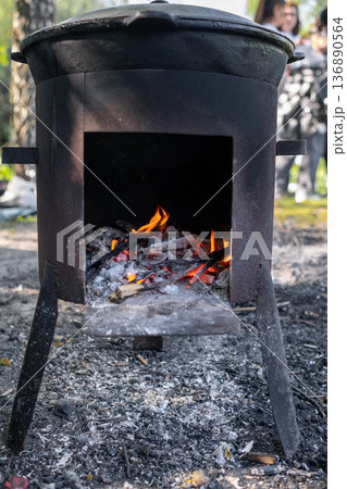Fire Burns Brightly in a Rustic Metal Stove While Wood is Added for Cooking Outdoors in a Natural Setting During Daytime Fire Burns Brightly in a Rustic Metal Stove While Wood is Added for Cooking Outdoors in a Natural Setting During Daytime 136890564
