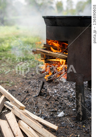 Wood Fire Cooking Pot Heating Over an Outdoor Flame With Stacked Firewood Nearby Wood Fire Cooking Pot Heating Over an Outdoor Flame With Stacked Firewood Nearby 136890608