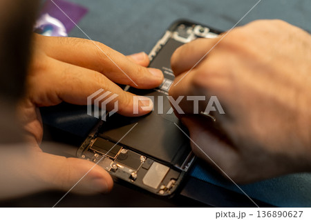 Phone Repair Technician Replacing Battery in Smartphone Inside Workshop During Daylight Hours 136890627