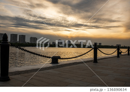 Sunset View Over the Calm River With City Skyline and Chain Barrier Along the Waterfront in an Urban Landscape 136890634