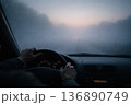 Driving on a Foggy Road at Dawn With Hands on the Steering Wheel and Dim Lights Ahead 136890749