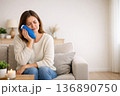 Woman Sitting on Couch With Blue Ice Pack on Face at Home While Experiencing Discomfort in Living Room During Daytime 136890750
