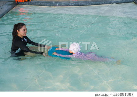 preschool child girl learning to swim with board with mother in swimming pool 136891397