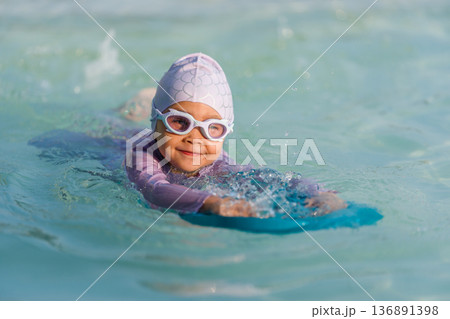 preschool child girl learning to swim with board in swimming pool 136891398