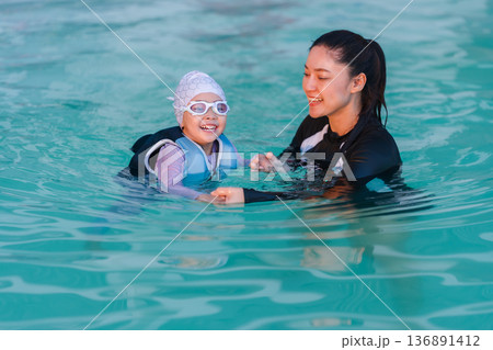 preschool child girl in life jacket learning to swim with mother in swimming pool 136891412