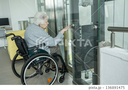 Senior woman in wheelchair entering glass elevator. Senior woman in wheelchair entering glass elevator. 136891475