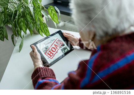 Old person recognizing fake news on digital tablet. 136891516
