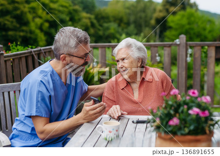 Caregiver spending time with elderly woman, showing her something in phone. 136891655