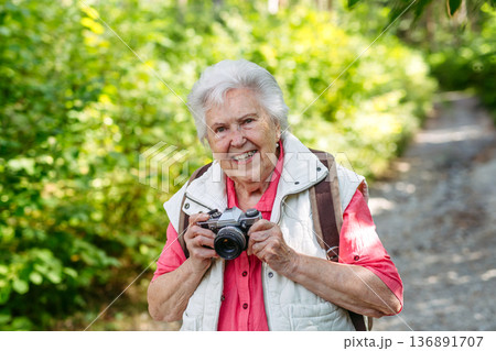 Elderly woman photographing nature during forest walk. 136891707
